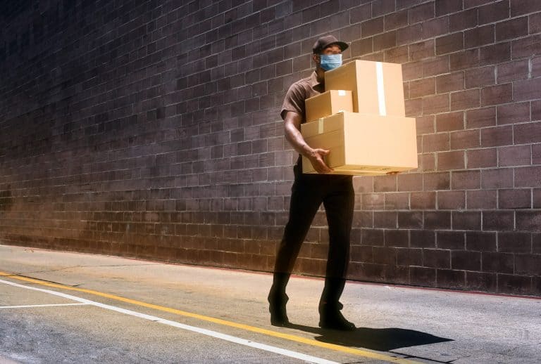 A delivery man carrying three parcels wearing a face mask