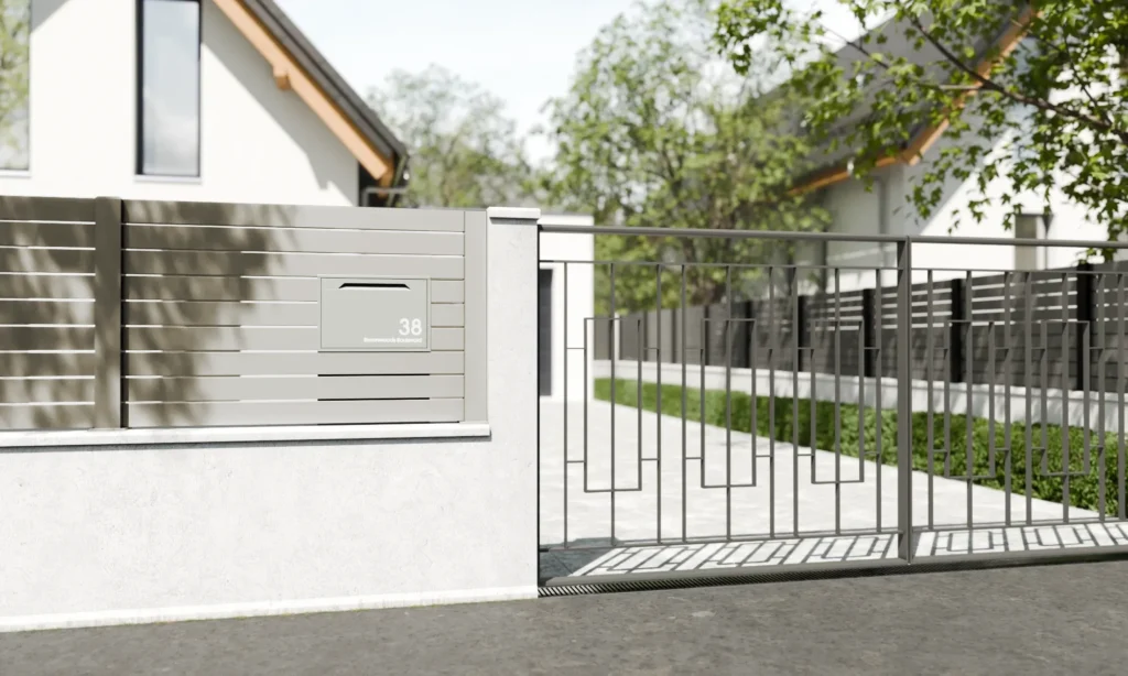 Pebble grey fence-mounted parcel box installed on a modern boundary fence beside a driveway entrance.
